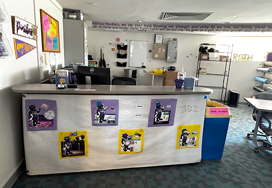 front desk with a walk up counter in a room with office supplies and UNI panther themed wall decorations.