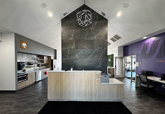 Front desk in a room with a vaulted ceiling, a coffee bar on the left, and a fitness room entrance on the right. 